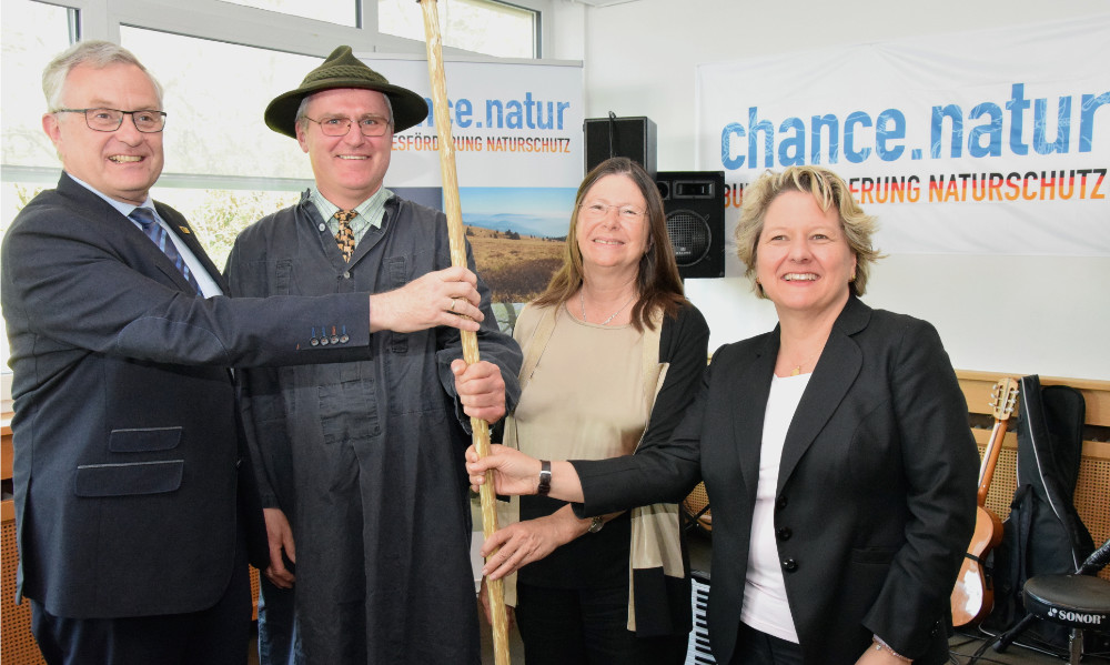 Gruppenfoto: Zwei Männer und zwei Frauen halten gemeinsam einen Hirtenstab. Im Hintergrund lesbar: "chance.natur"